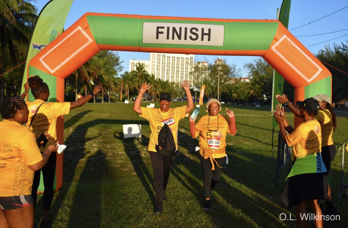 Two Global Sun Integration walkers cross the finish line with arms raised as teammates cheer